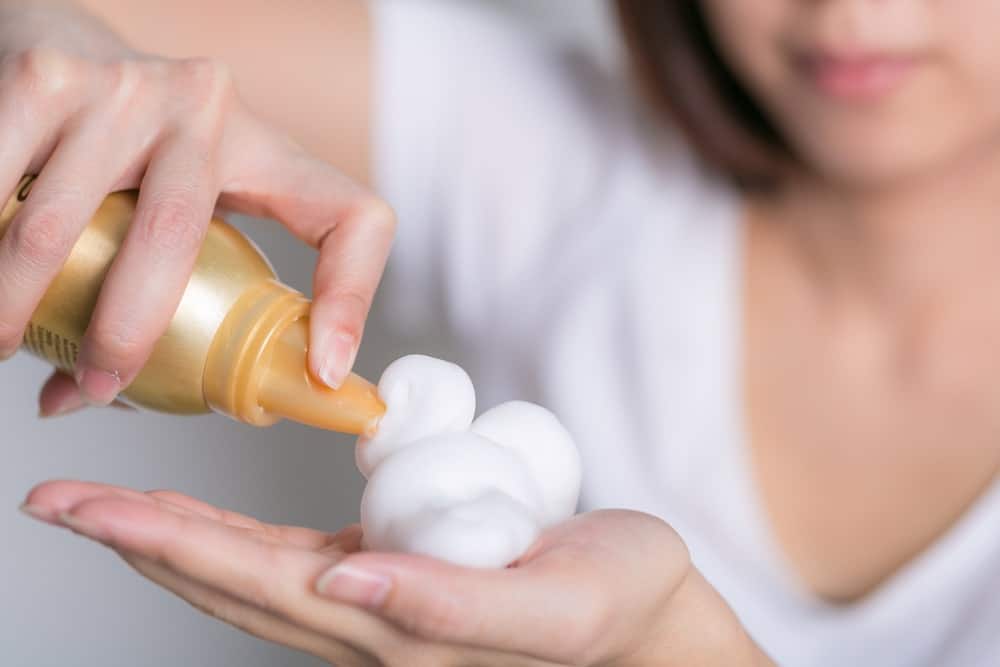 Hairstylist squeezing mousse spray on hand.