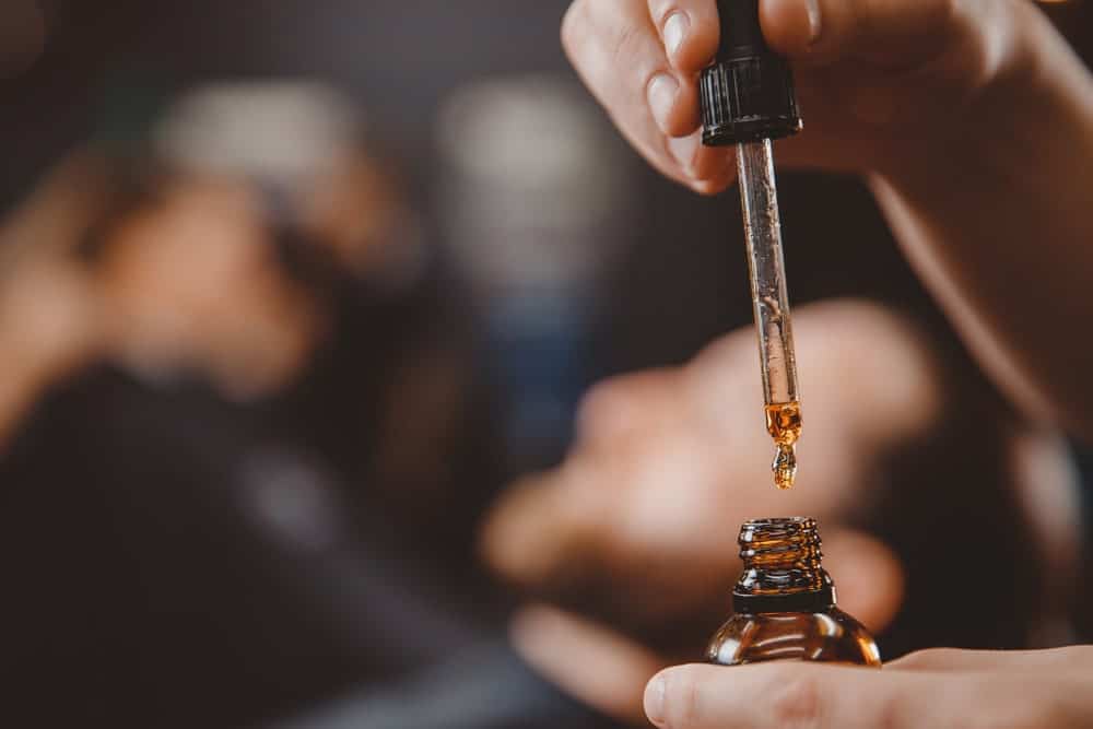 Hand holding a dropper and bottle of beard oil.