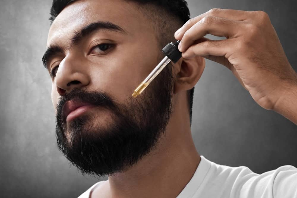 A bearded man applying coconut oil to his beard.