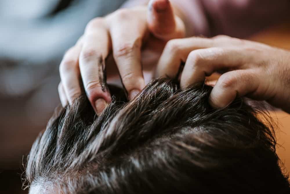 Barber applying black hair pomade on a man.