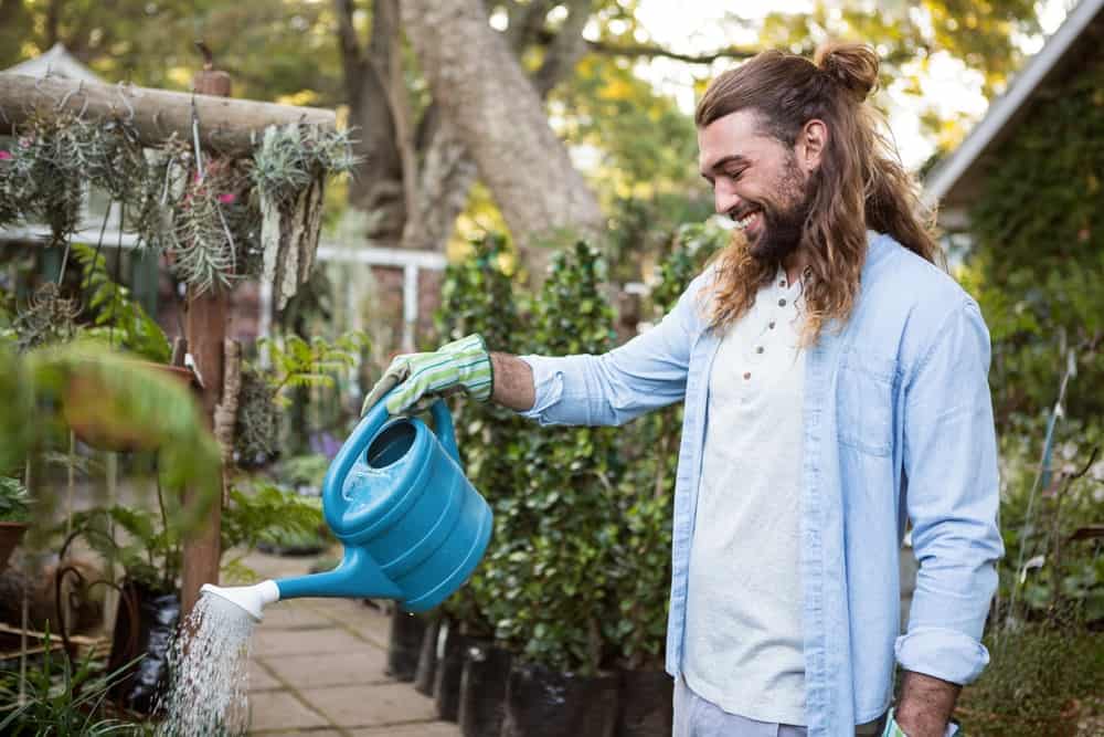 The man smiles while watering the plants in the garden.