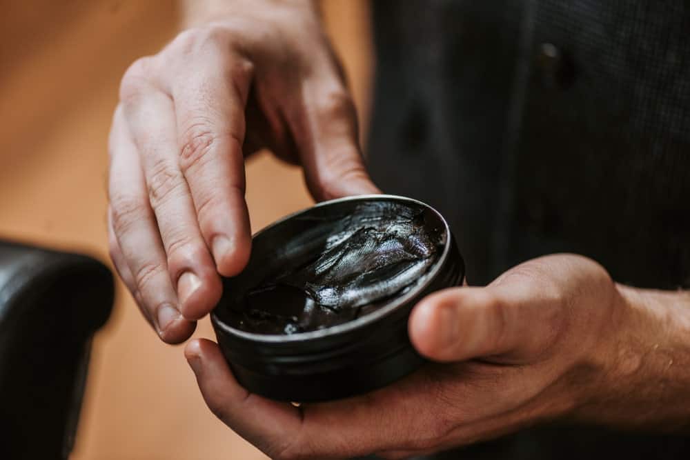 Man holding black pomade jar.