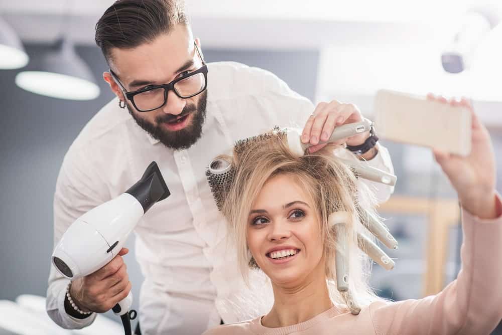 A blond woman taking a selfie with her hair stylist.