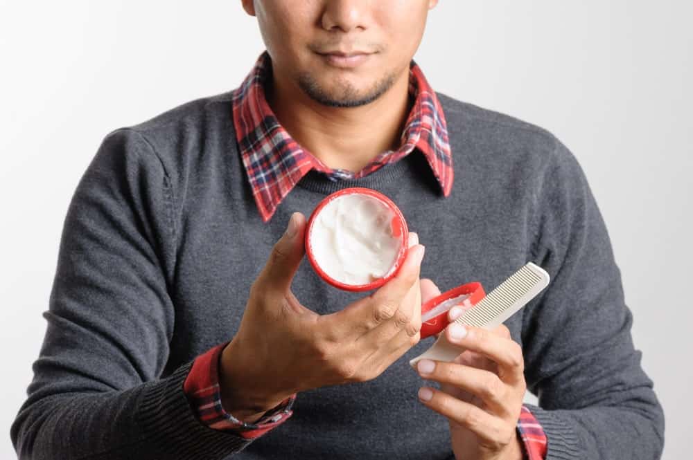 Man holding a tub of wax and a comb.