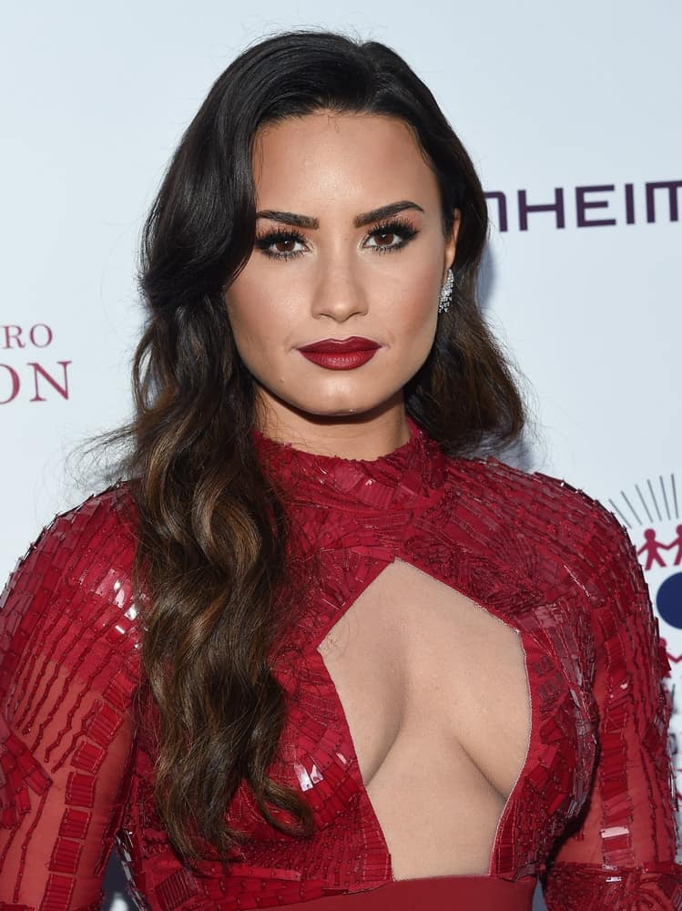 Demi Lovato flaunted her lovely red lips with her red dress and beautiful side-swept wavy hairstyle with highlights and side-swept bangs at the 2017 Brent Shapiro Foundation Summer Spectacular on September 9, 2017 in Beverly Hills, CA.