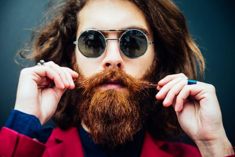 Bearded man in a red formal suit with sunglasses and a full beard.