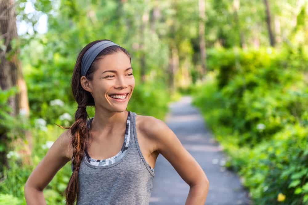 A woman wearing a gray sweatband at a jogging trail.