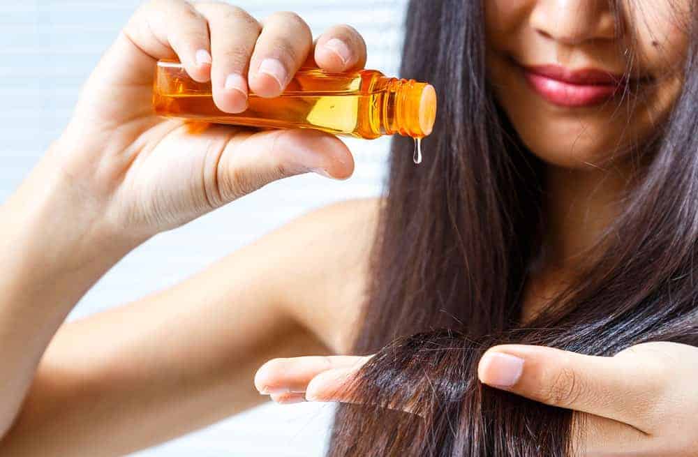 Woman applying some oil on her long hair.