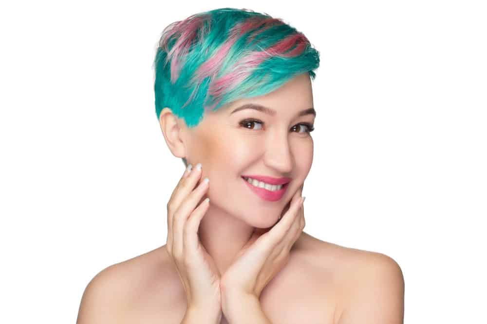 Beautiful woman with short dyed hair smiles and touches her face.