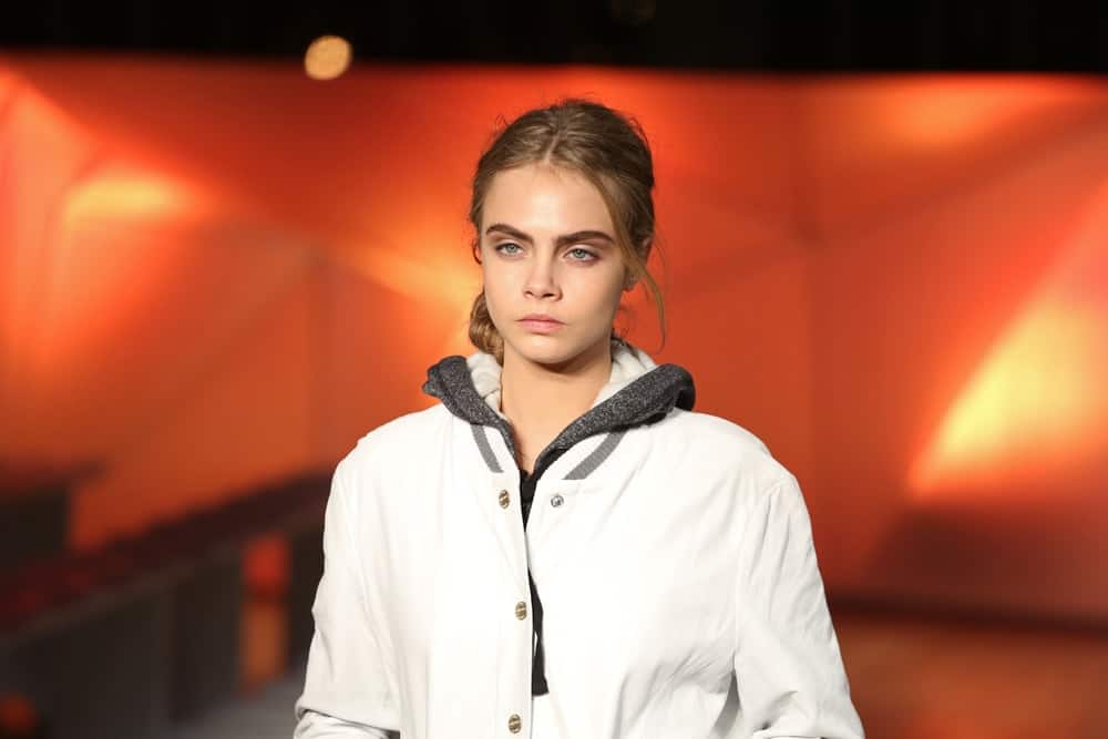 Cara Delevingne was dressed in a white coat that paired well with her loose and messy low bun hairstyle with loose tendrils at the Matthew Williamson, part of London Fashion Week, A/W 2013 in London, England on February 17, 2013.