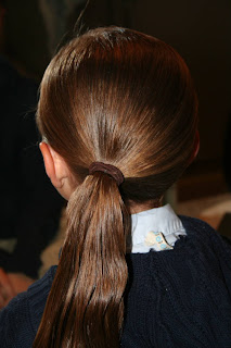 Back view of young girl's hair being styled into "Ponytail Half Braid"