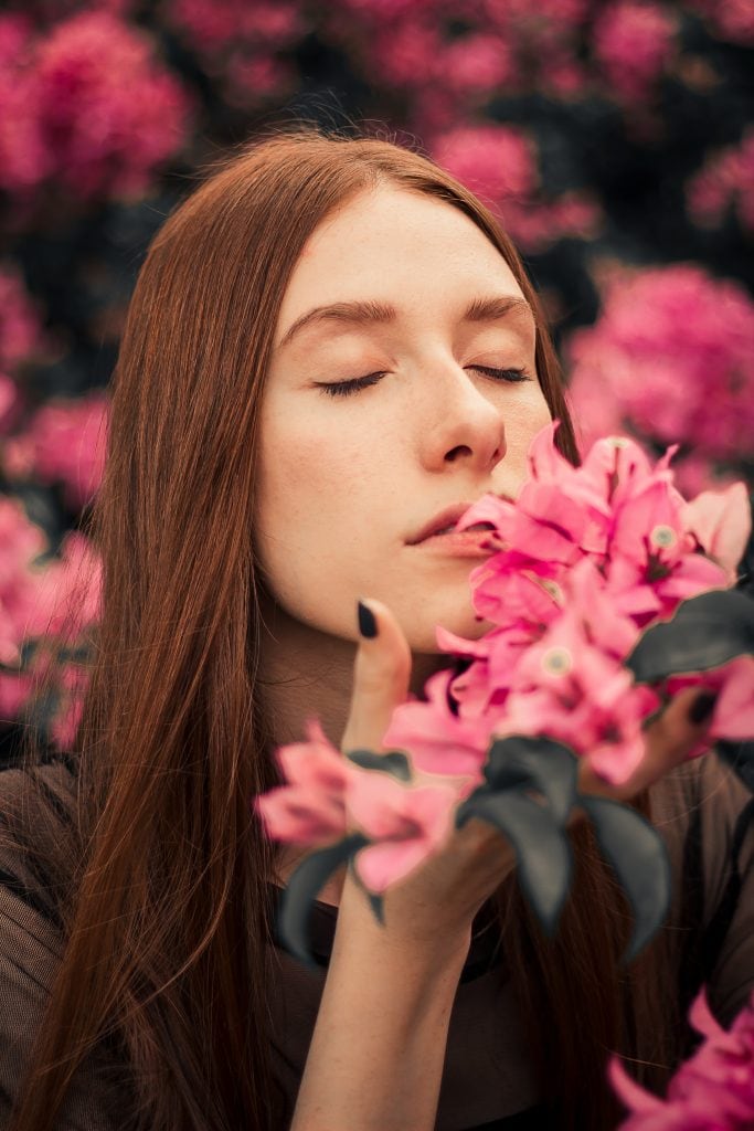 Close-up shot of woman with curly hair smelling pink flowers