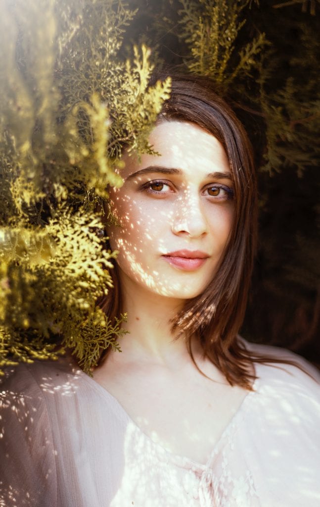 Close-up shot of woman with straight hair standing amongst leaves.