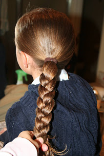 Back view of young girl's hair being styled into "Ponytail Half Braid"