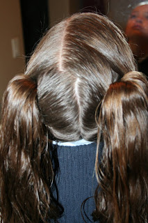 Back view of a young girl's hair being styled into “Two Hearts Twist” hairstyle