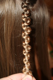 Close up view of young girl's hair being styled into "Teen Slide-Up Braid" hairstyle outside