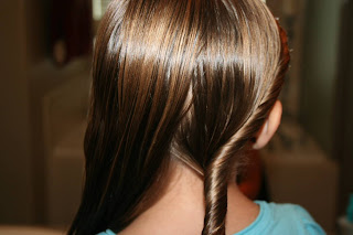 Back view of a young girl having her hair styled into “Double-twist" ponytail