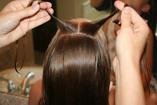 Back view of young girl's hair being styled into "Knots into Side Ponytail" hairstyle