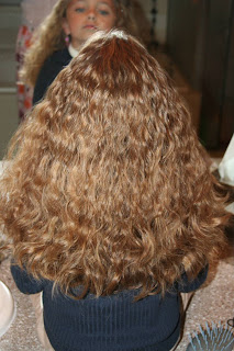 Back view of young girl's hair being styled into "Curls After Triple Twists w/ Messy Buns" hairstyle