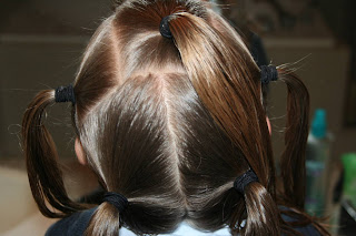 Back view of young girl's hair being styled into "Holiday Twisty Buns" hairstyle