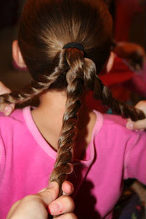 Back view of young girl's hair being styled into "Triple-Twist Ponytail' hairstyle