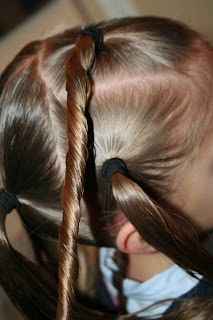 Side view of young girl's hair being styled into "Holiday Twisty Buns" hairstyle