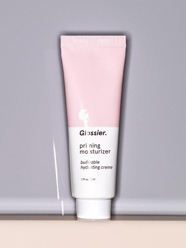 Photo of Glossier Priming Moisturizer resting on a beige surface against a gray background