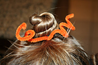 Close up view of young girl's hair being styled into "Holiday Twisty Buns" hairstyle with an orange pipe cleaner