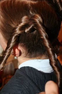 Side view of a young girl's hair being styled into “Two Hearts Twist” hairstyle