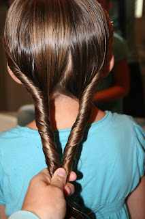 Back view of a young girl having her hair styled into “Double-twist" ponytail