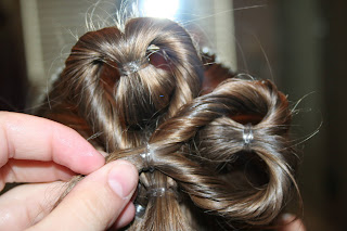 Back view of young girl's hair being styled into "Three-Leaf Clover Twists" hairstyle