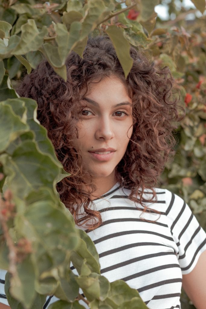 Close-up shot of woman with curly hair standing amongst leaves