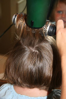 Back view of young girl's hair being styled with a blow dryer and round brush