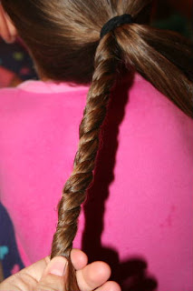 Back view of young girl's hair being styled into "Triple-Twist Ponytail' hairstyle