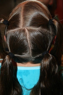 Back view of young girl's hair being styled into "4 Messy-Pigtail Twists" hairstyle