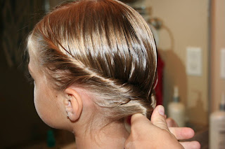 Side view of a young girl having her hair styled into “Double-twist" ponytail