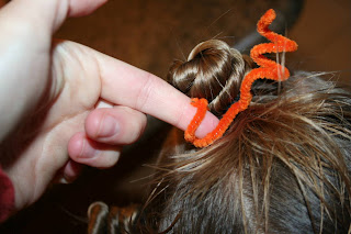 Close up view of young girl's hair being styled into "Holiday Twisty Buns" hairstyle with an orange pipe cleaner