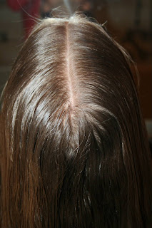 Back view of a young girl's hair being styled into “French Designer Heart” hairstyle