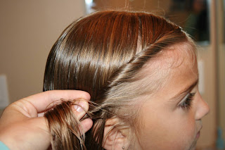 Side view of a young girl having her hair styled into “Double-twist" ponytail