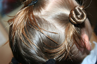 Side view of young girl's hair being styled into "Holiday Twisty Buns" hairstyle