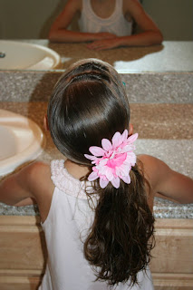 Back view of young girl outside modeling "Knots into Side Ponytail" hairstyle styled with floral hair accessory