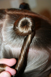 Side view of young girl's hair being styled into "Holiday Twisty Buns" hairstyle