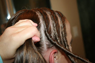 Side view of Young girl's hair being styled into "Triple Twists and Messy Buns"